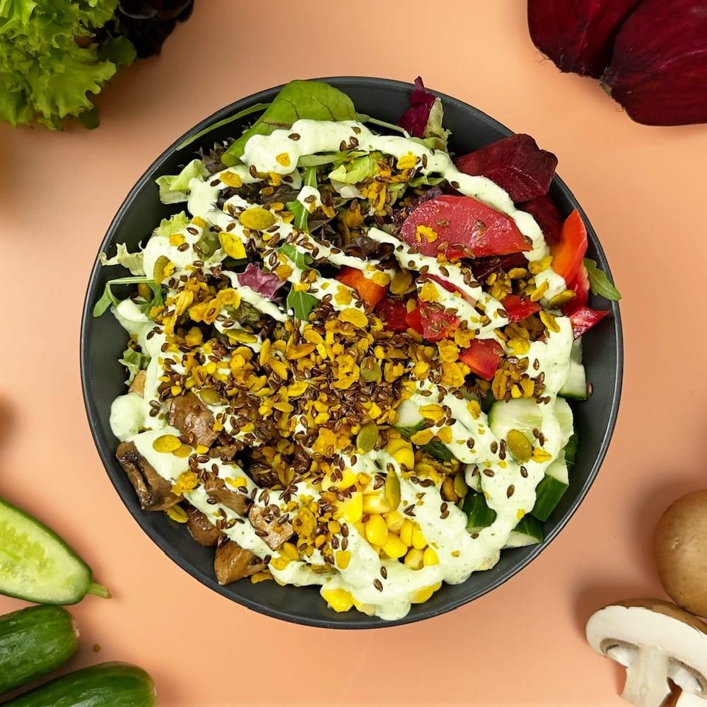 Wähle aus den unseren Bowls: FRÜHLINGS BOWL mit Couscous, Mais, Gurke, Salat-Mix, gebratene Champignons, Wurzelgemüse und Kernmix mit Petersilien Quark Dressing.